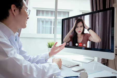 Asian doctor video conference with woman patient care discussing and consultant for medical coronavirus video call user interface healthcare online service remotely talking when quarantine at home.の写真素材