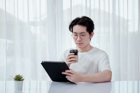 Asian man working from home with tablet self isolation from society to reduce risk, quarantine...