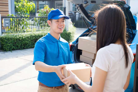 Delivery service male in uniform give cardboard box package to receiver customer client front home, fast express offsite when crisis coronavirus, covid19 new normal lifestyle concept.の写真素材