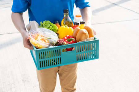 Food Deliver Asian man in blue uniform give fruit and vegetable to receiver customer front house, fast express grocery service when crisis coronavirus, covid19 new normal lifestyle concept.の写真素材