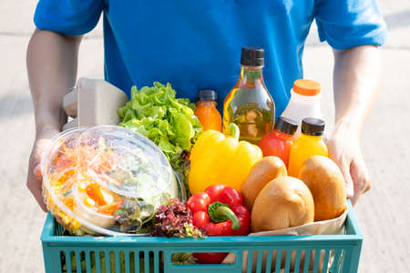 Food Deliver Asian man in blue uniform give fruit and vegetable to receiver customer front house, fast express grocery service when crisis coronavirus, covid19 new normal lifestyle concept.の写真素材