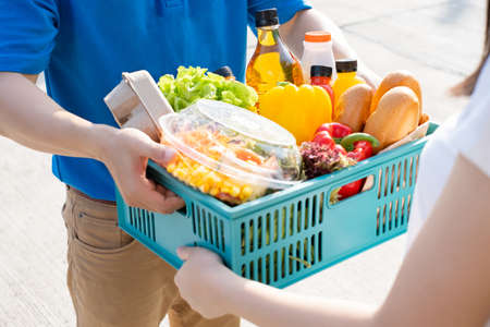 Food Deliver Asian man in blue uniform give fruit and vegetable to receiver customer front house, fast express grocery service when crisis coronavirus, covid19 new normal lifestyle concept.の写真素材