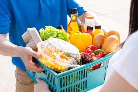 Food Deliver Asian man in blue uniform give fruit and vegetable to receiver customer front house, fast express grocery service when crisis coronavirus, new normal lifestyle concept.の写真素材