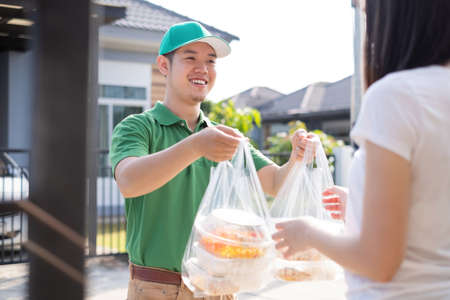 Food Delivery man wearing mask handing plastic bags shopping online from supermarket to female client service customer front house, express grocery when coronavirus covid19 new normal lifestyle.の写真素材