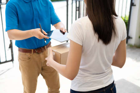 Delivery service male in uniform give cardboard box package to receiver customer client front home, fast express offsite when crisis coronavirus, new normal lifestyle concept.の写真素材