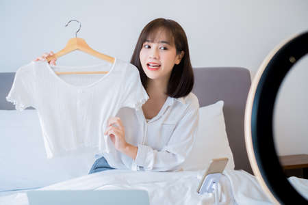 Beautiful Asian woman vlogger recording dressing up of clothes hanging on a hanger in the wardrobe, Modern businesswoman using social media for marketing.の写真素材