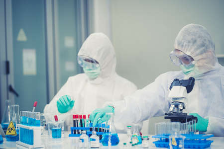 Group of Scientists with a microscope in laboratory, developing a vaccine. They Work in an...