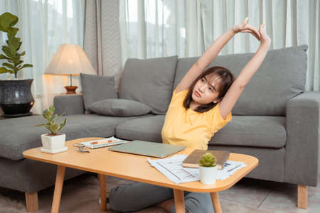Young asian woman tried to lying stretching after working with laptop computer on couch at the living room relax from hard work at home.の写真素材