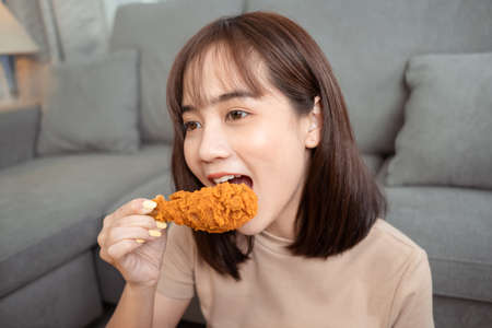 Young asian woman takeaway eating junk food chicken nuggets wing, Female having fun enjoying fast food delivery service safe and stop coronavirus spread by social distancing concept.の写真素材