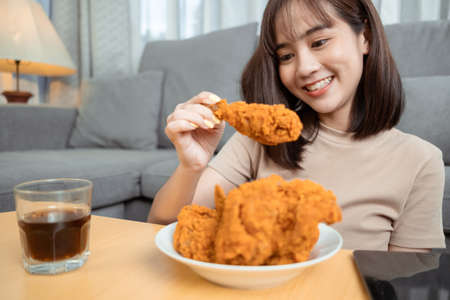 Young asian woman takeaway eating junk food chicken nuggets wing, Female having fun enjoying fast food delivery service safe and stop coronavirus spread by social distancing concept.の写真素材