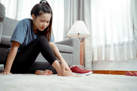 After workout of Young asian woman sitting foot pain between to exercise at home in the living room,...