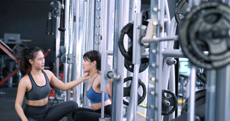 Sporty asian women exercise workout squats at fitness gym with the barbell in smith machine,...