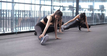 Group of sporty young asian women in sportswear warming up with gymnastics and stretching exercises pre-workout weight training, healthy bodybuilding, Athlete builder muscles lifestyle concept.の写真素材