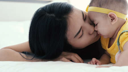 Asian mother in diaper playing with her's baby on bed in bedroom, Family having fun together, Young mother cuddling baby woman and new born relax breast feeding baby concept.の写真素材