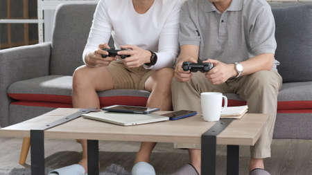 Asian two age generations men family old father embracing young adult son having fun enjoying play video game funny video using at home sit on sofa. Happiness Asian family concepts.の写真素材