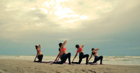 Group females yoga practice in class on mat stretching relaxation exercise with pose fitness sport for healthy on the beach and seaside at sunset relax holiday vacation time in summer.の写真素材