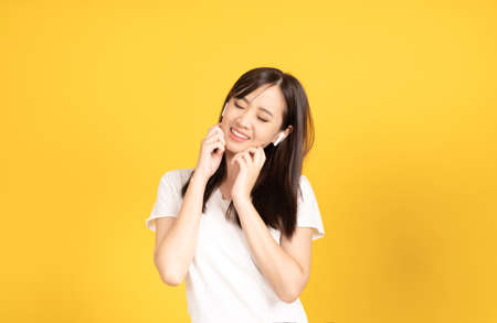 Happy smiling asian young girl with earphones listening music with cheerful expression and looking at camera over yellow background. Facial expression concept.の写真素材