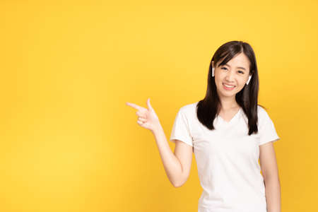 Happy smiling asian young girl with earphones listening music with cheerful expression and looking at camera over yellow background. Facial expression concept.の写真素材
