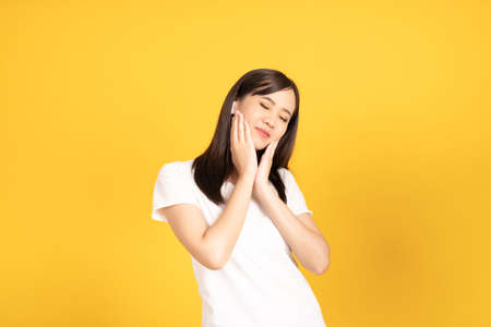 Happy smiling asian young girl with earphones listening music with cheerful expression and looking at camera over yellow background. Facial expression concept.の写真素材