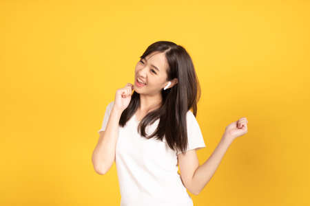 Happy smiling asian young girl with earphones listening music with cheerful expression and looking at camera over yellow background. Facial expression concept.の写真素材