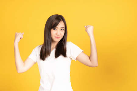 Happy asian young woman showing strength gesture with arms, symbol of feminine power and looking at camera yellow isolated on background with copy space.Look at my muscles!の写真素材