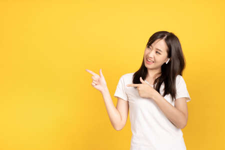 Happy smiling asian young girl with earphones listening music with cheerful expression and looking at camera over yellow background. Facial expression concept.の写真素材