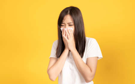 Asian young woman wearing white t-shirt standing and crying wipe the mucus with tissue, She sneezing sinus using towel to wipe snot from nose at studio shot on yellow background.の写真素材