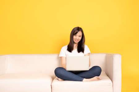 Young asian woman relaxing on comfortable couch, using laptop at home, She is happy to spend some free time online while chatting with friends in social network, shopping or working online.の写真素材