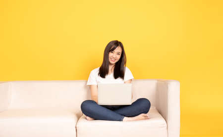 Young asian woman relaxing on comfortable couch, using laptop at home, She is happy to spend some free time online while chatting with friends in social network, shopping or working online.の写真素材