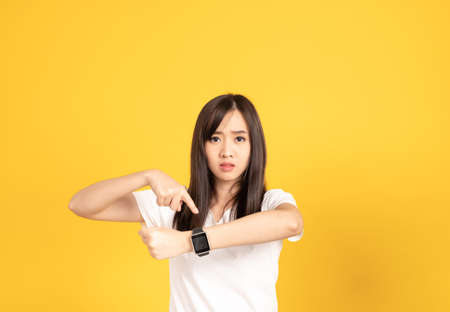 Asian young woman wearing white t-shirt standing. She looking on smart watch on hand put hand on cheek at studio shot on yellow background. People lifestyle concept.の写真素材