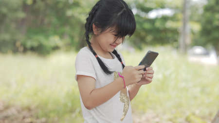Little cute asian girl playing smartphone chatting with friends smiling enjoy outdoor alone happy lifestyle concept.の写真素材