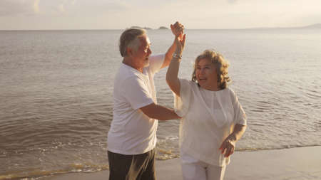 Asian couple senior elder retire resting relax dancing at sunset beach honeymoon family together happiness people lifestyle.の写真素材