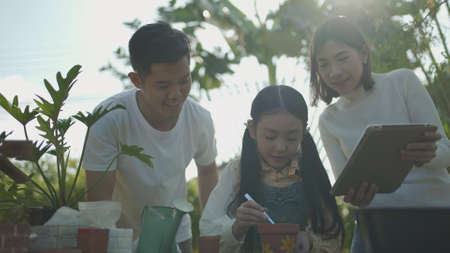 Asian couple with daughter gardening while watching laptop together in the backyard garden. Happy...