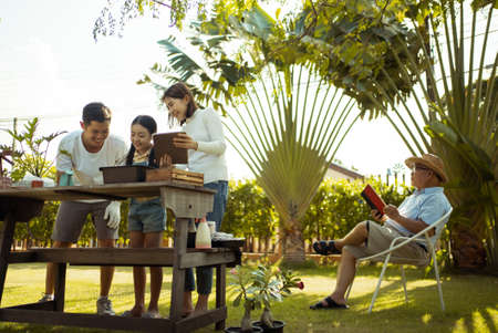 Asian couple with daughter gardening while watching laptop together in the backyard garden. Happy family gardening together and taking care of nature. People and ecology concept.の写真素材