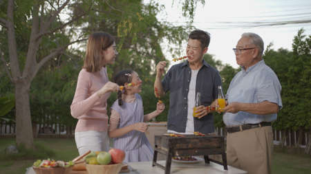 Happy asian family dining and tasting juice on glasses in barbecue dinner party, Multi generation family enjoying meal together. People having outdoor party eating food at backyard home in garden.の写真素材