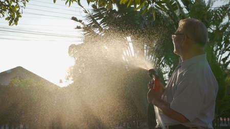 Happy asian senior grandpa pouring water from a hose. Funny Grandparent and grandchild playing with...