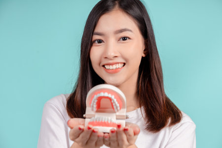 Dental of asian woman with tooth sample and white teeth increase confidence for healthy on blue background isolated studio shot, Happiness teenager smiling facial expression.の写真素材