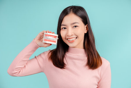 Dental of asian woman with tooth sample and white teeth increase confidence for healthy on blue background isolated studio shot, Happiness teenager smiling facial expression.の写真素材