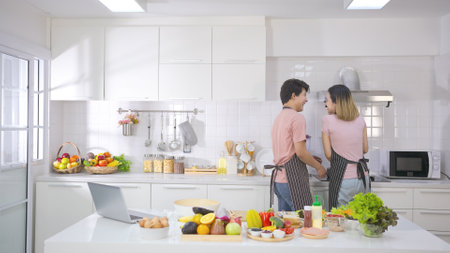 Young asian man happy help his girlfriend cook in kitchen with happiness and smile enjoy life together in home kitchen. Young people relationship and lifestyle. Family concept.の写真素材