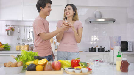 Two couple young asian drinking vegetarians fresh smoothie and smile enjoy life together in home kitchen. Young couple in the morning preparing meal together with affection and love.の写真素材