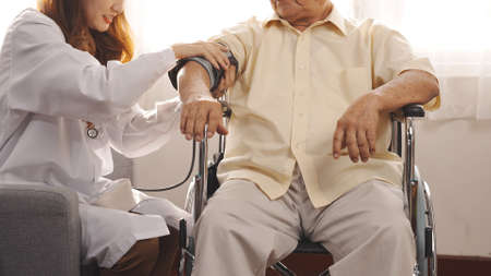 Female nurse doctor in uniform health check measuring blood pressure senior grandfather patient at home medical visit, Elderly old male people healthcare support and encouraging the patient in life.の写真素材