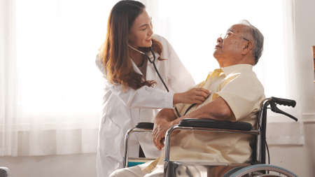Female nurse doctor in uniform health check senior grandfather patient at home medical visit,...