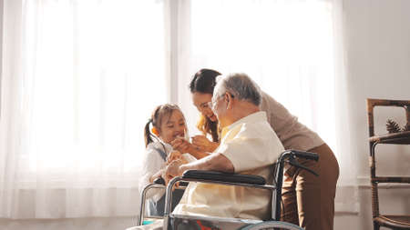 Happy Family Multi-generation Mother and daughter taking care of the senior granddfather in the house, sitting on the wheelchair happiness, Elderly retirement concept.の写真素材