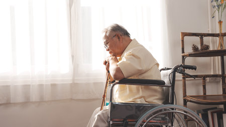 Elderly Senior male stay home after retirement alone at home unhappily and lonely his looking out the window with wheelchair and cane.の写真素材