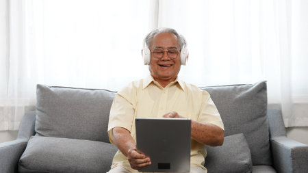 Happy Senior male using laptop computer listening enjoy music song in online streaming digital technology wifi internet connection, Elderly retired life at home concept.の写真素材