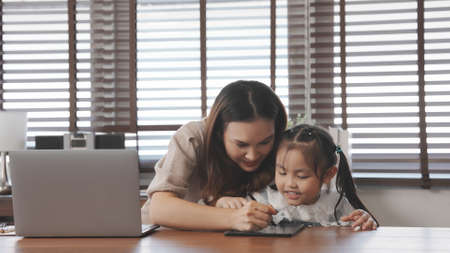 Asian mother teaching daughter help drawing togther after back form school at home, Mother working using laptop computer digital technology.の写真素材