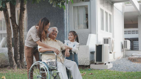 Happy Family Grandfather on weelchair with mother and daughter looking around in the backyard outdoor at home, Elderly senior health care concept.の写真素材