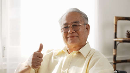 Happy senior male smiling and thumbs up in the house, sitting on the wheelchair happiness, Elderly retirement insurance health concept.の写真素材