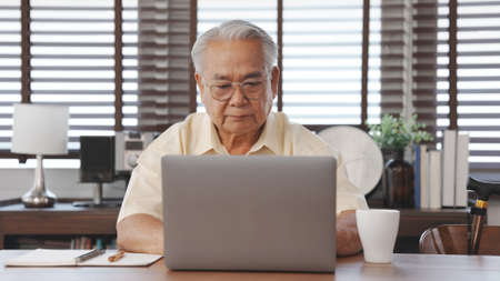 Happy Senior male using laptop searching for health insurance online website on laptop computer buying insurance fot retirement sitting at home, Elderly healthy lifestyle concept.の写真素材