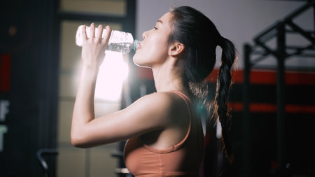 Athlete Asian Woman Drinking Pure Water After Workout Exercise or Training Building Muscles and Burning Fat Cardio, Refresh Body Healthy Lifestyle in Fitness Gym.の写真素材